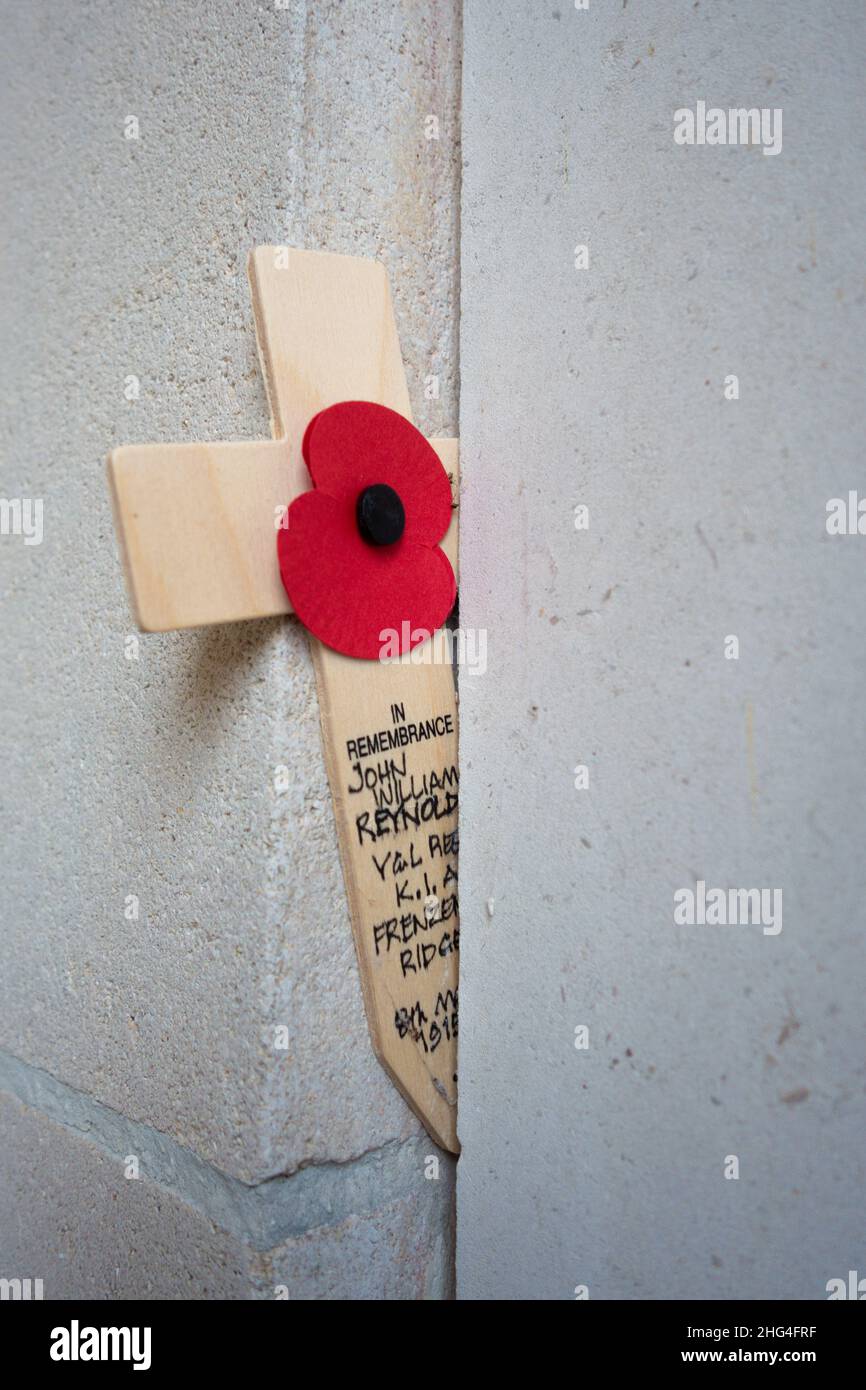 Un papavero artificiale su una croce si trova davanti alle iscrizioni con i nomi dei soldati caduti alla porta Menin a Ypres, Belgio. Foto Stock