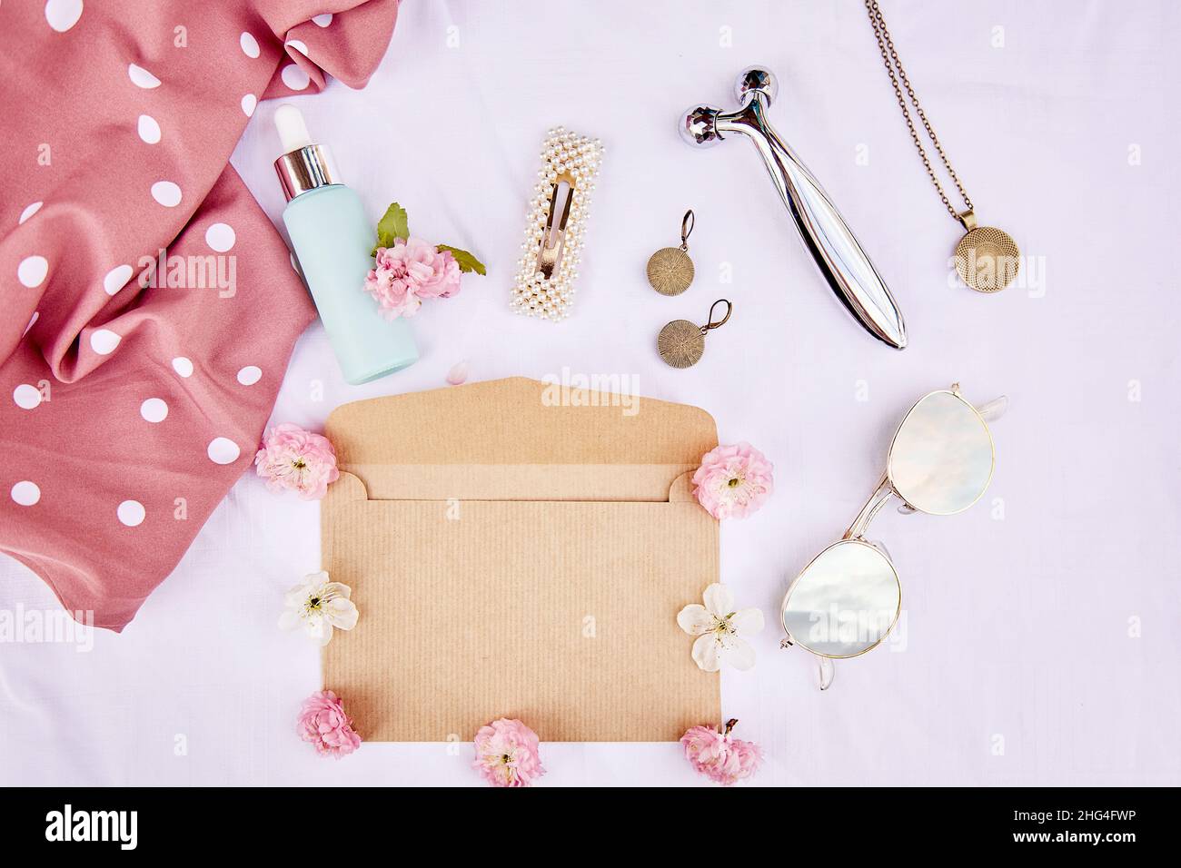 Busta primavera femminile mock up con fiori rosa, occhiali da sole con riflesso cielo, accessori, massaggiatore, regalo cosmetico su tessuto sfondo bianco. 8 del concetto di marzo. Foto Stock