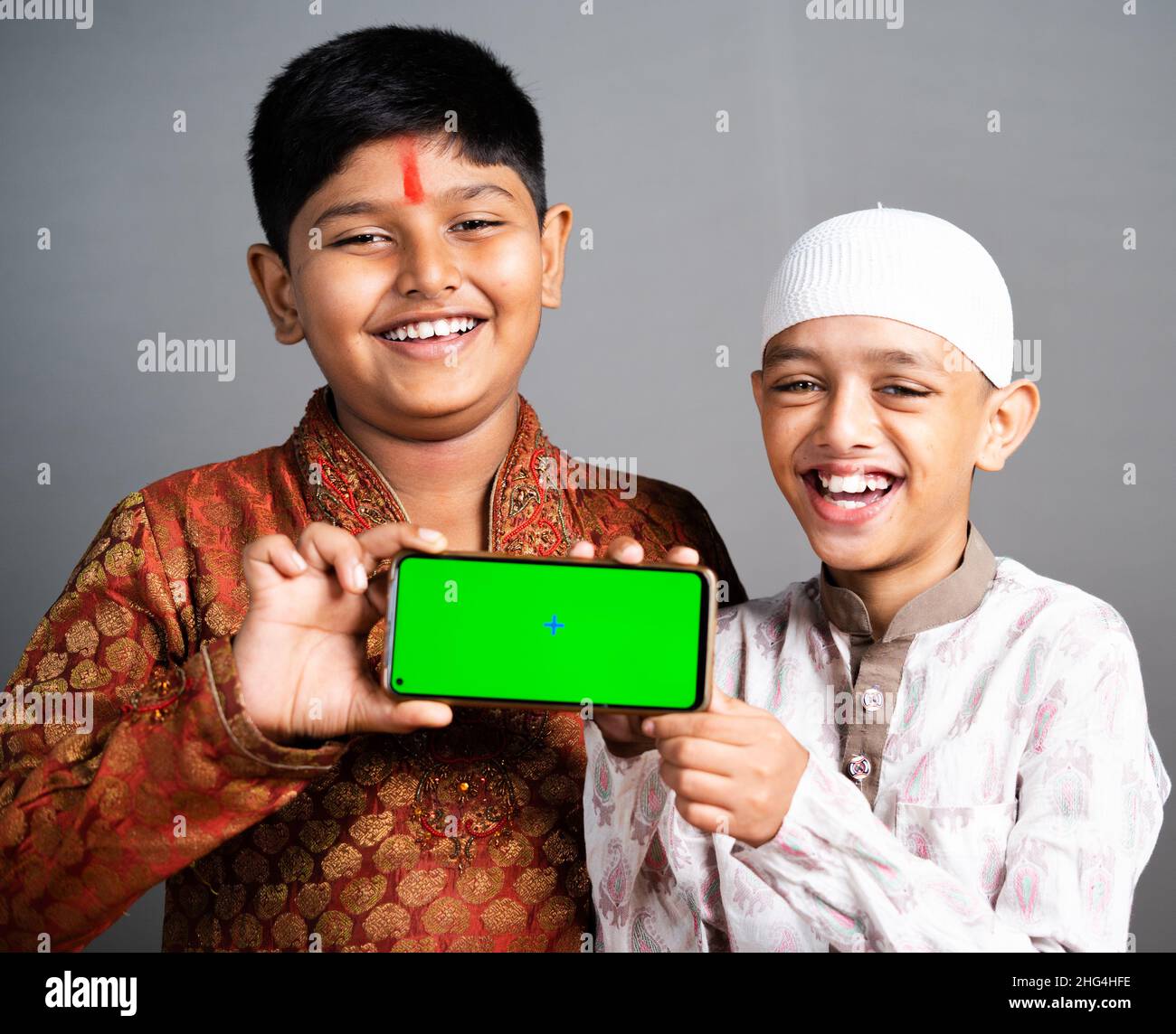 Felice sorridente multi etnico indiano religioso ragazzi che tengono mobile con schermo verde su sfondo grigio - concPET di promozione di pubblicità di applicazione Foto Stock