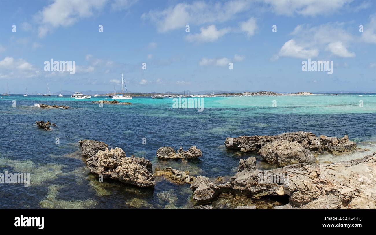 Vista panoramica da una spiaggia rocciosa di Formentera, Spagna, sullo sfondo barche a vela ormeggiate sul cielo blu. Foto Stock