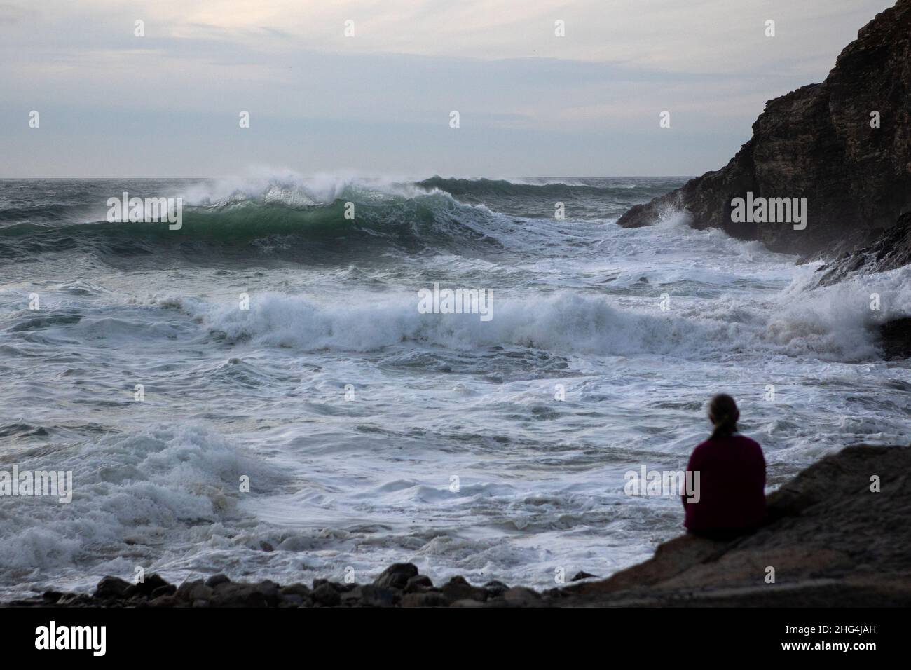 Una donna guarda come le onde arrivano dalle ondate atlantiche alla spiaggia di Chapel Porth sulla costa settentrionale della Cornovaglia Foto Stock