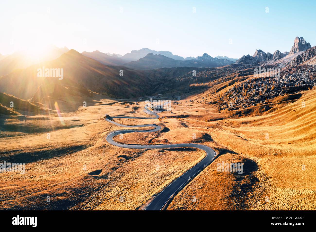 Fantastica vista aerea sulla strada tortuosa in autunno valle di montagna al tramonto. La luce dorata del tramonto illumina le montagne e l'erba arancione. Passo Giau, Alpi dolomitiche, Dolomiti, Italia Foto Stock