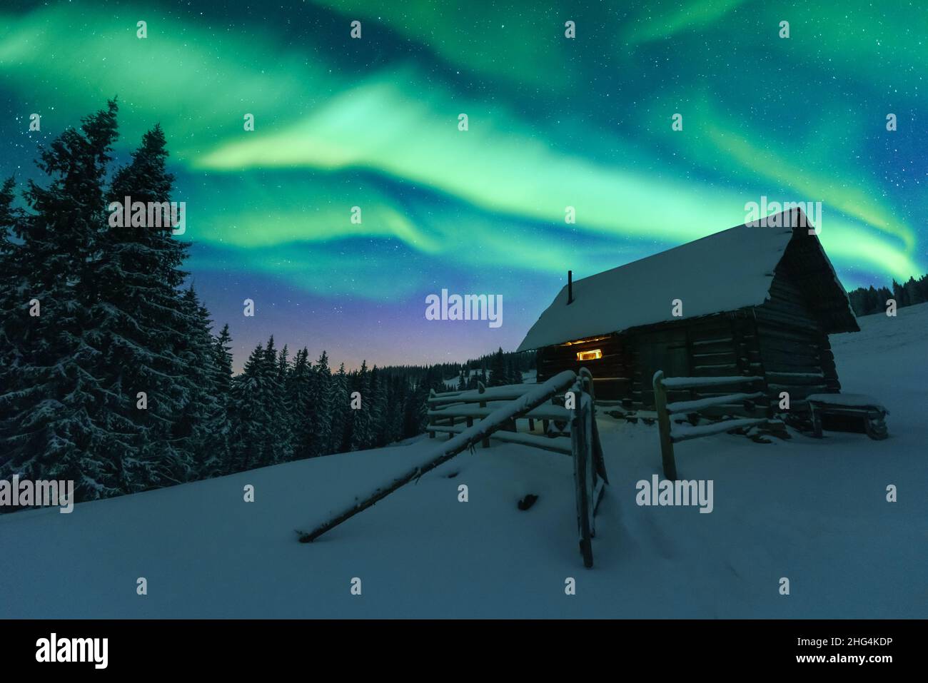 Fantastico paesaggio invernale con casa in legno con luce nella finestra in montagne innevate e northen luce nel cielo notturno. Vacanze di Natale e le vacanze invernali concept Foto Stock