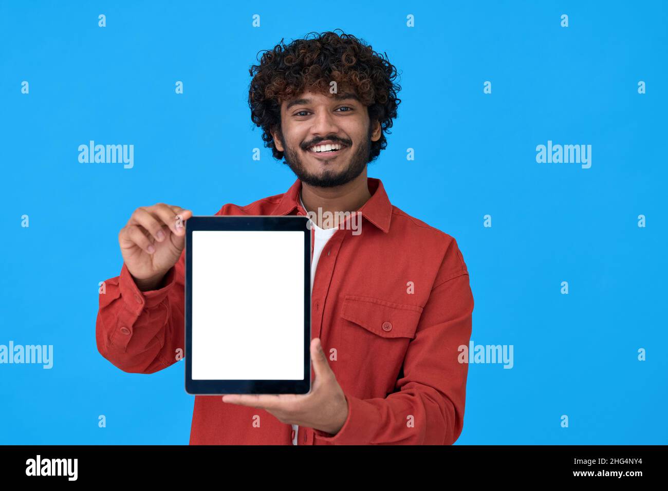Felice giovane indiano ragazzo mostrando grande schermo mockup tablet su sfondo blu. Foto Stock