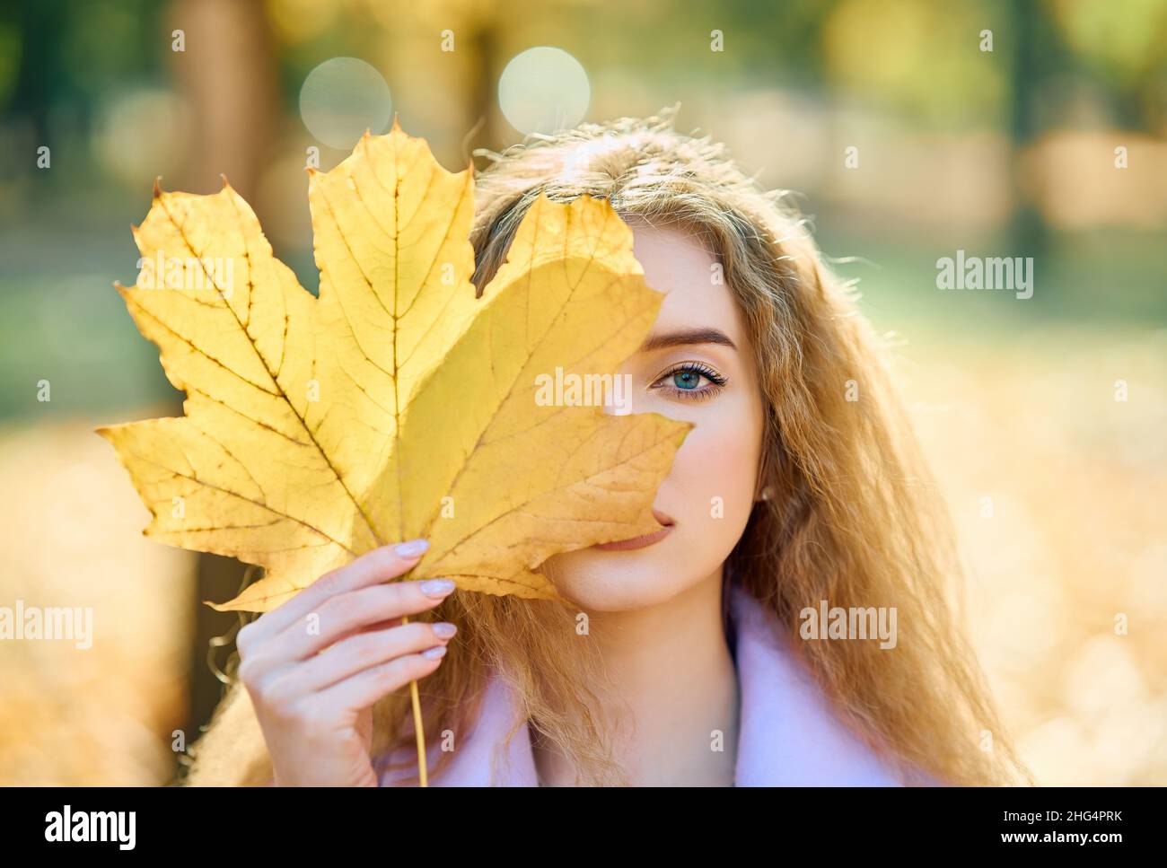 Autunno ritratto donna che tiene in mano giallo foglie di acero che copre il suo occhio su fondo natura caduta Foto Stock