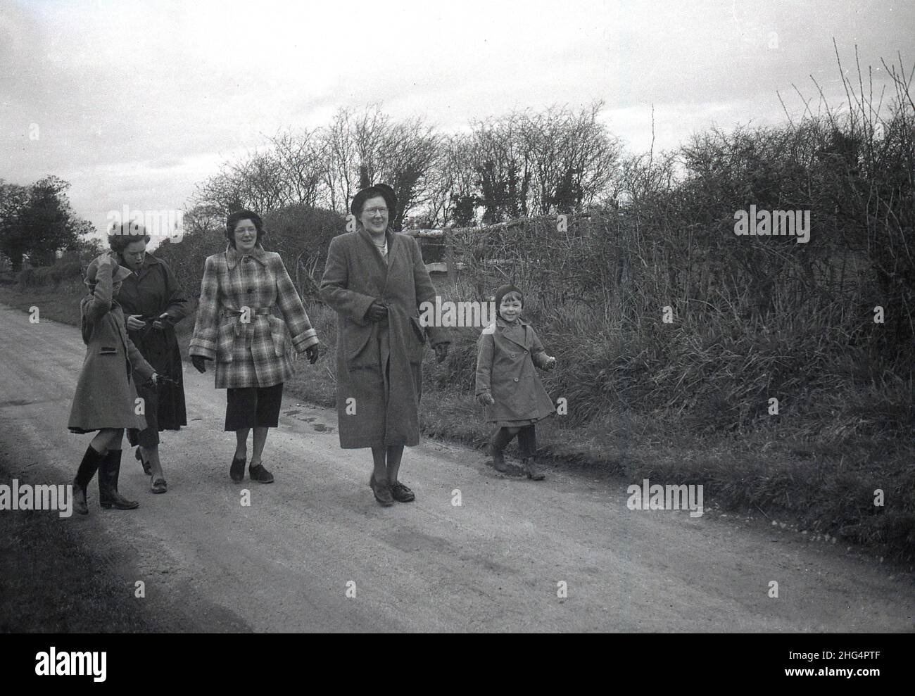1950s, storica, fuori su una pista o una corsia rurale, due madri e una nonna, indossando cappotti per una passeggiata diurna con i loro figli, due ragazze giovani, entrambe indossando wellies, Inghilterra, Regno Unito. Foto Stock