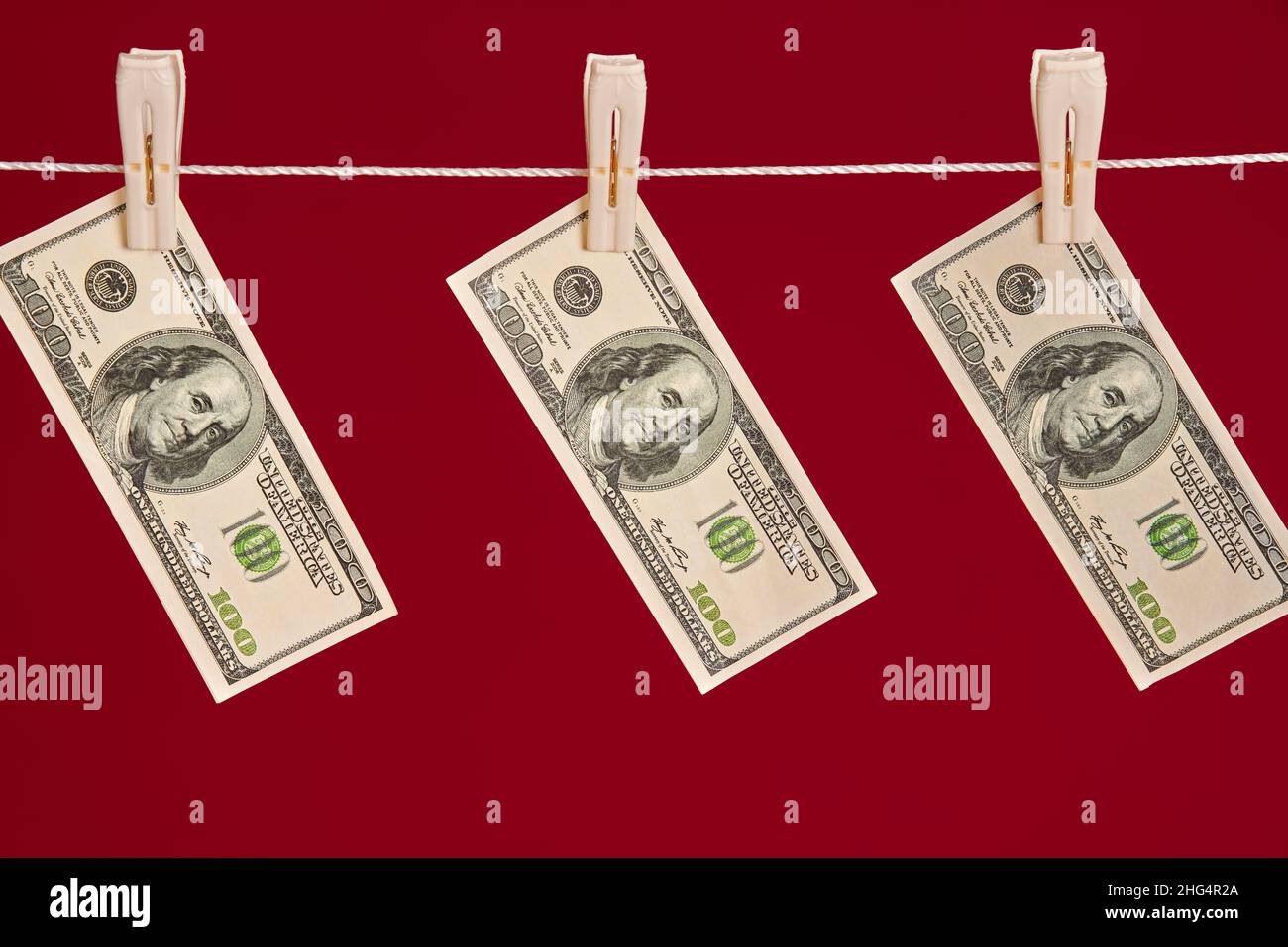 Riciclaggio di denaro, dollari americani appesi sulla corda su sfondo rosso studio. Finanza, corruzione, concetto di attività criminale Foto Stock