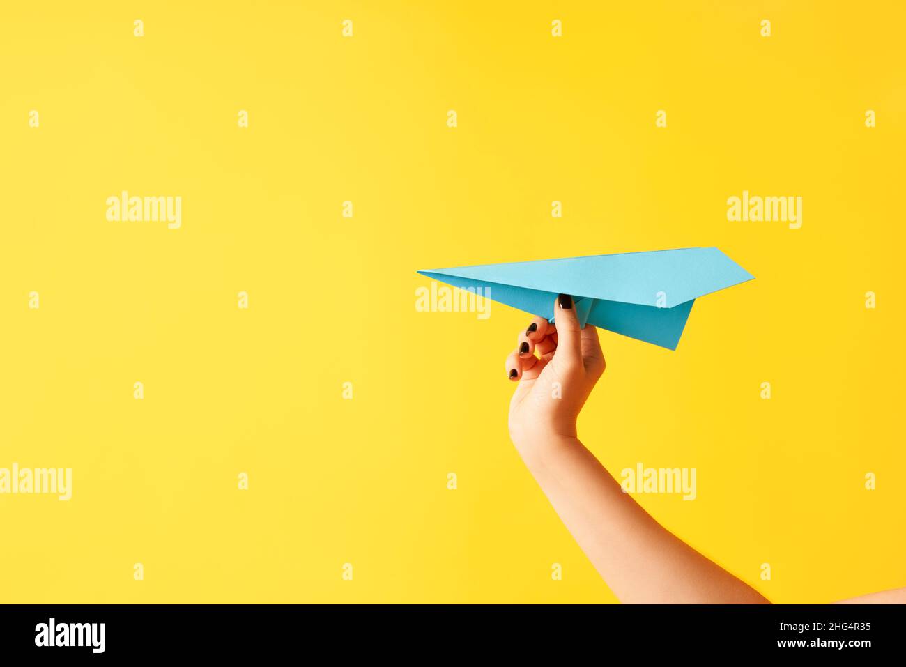 Una mano di donna tiene velivolo di carta blu su sfondo giallo con spazio di copia Foto Stock