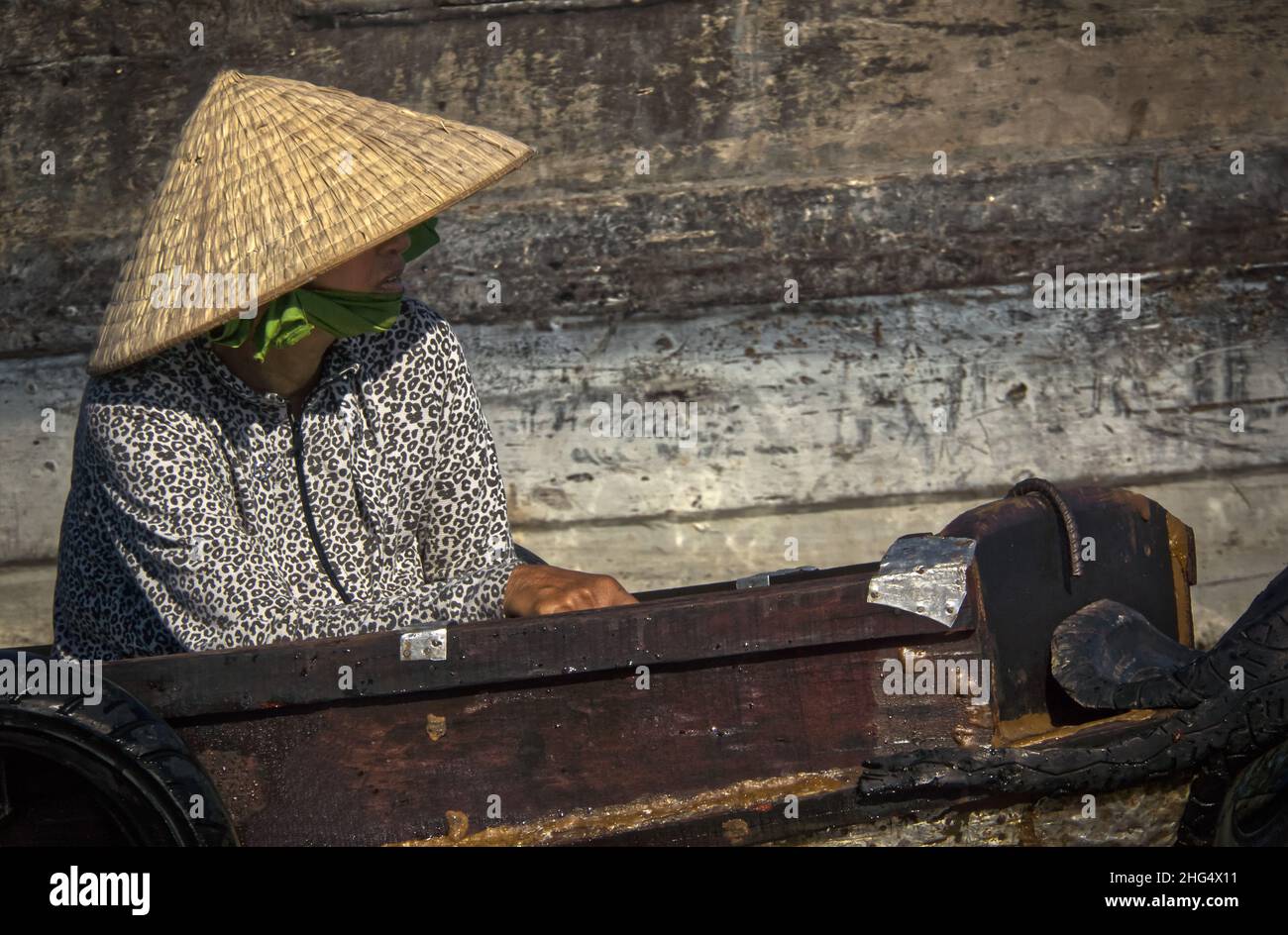 Eine ältere Vietnamesin mit Reishut sitzt in einem kleinen Holzboot auf dem Schwimmenden Markt von Cai Rang in der Nähe von Can Tho Foto Stock