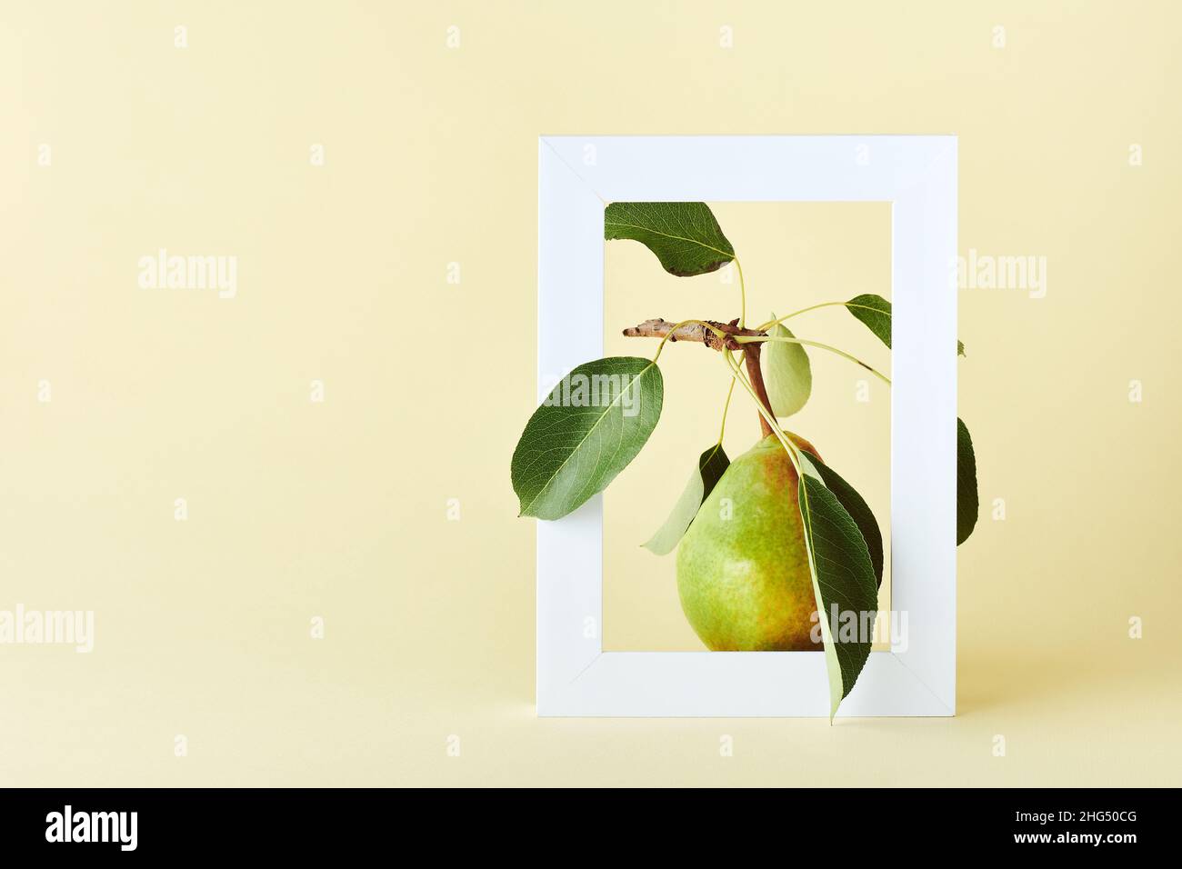 Pera matura con foglie in cornice bianca su sfondo giallo. Il concetto creativo della frutta estiva. Foto Stock