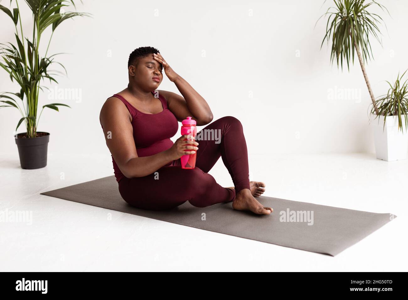 Esausta donna in sovrappeso seduta sul materassino fitness Foto Stock