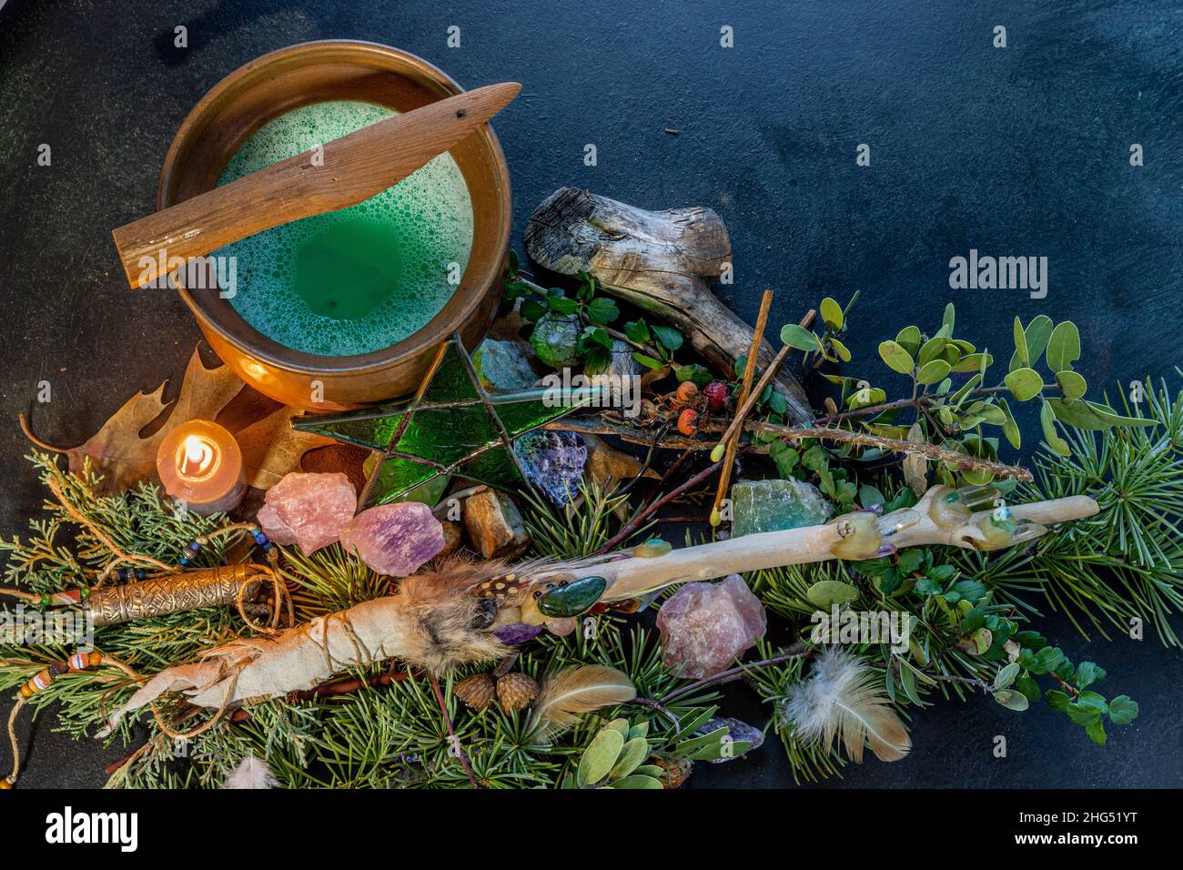 Calderone di rame pieno di pozione verde gorgogliante , una bacchetta magica con cristalli, candela che brucia, erba lora, oscura storia della strega, piatto occulto Foto Stock