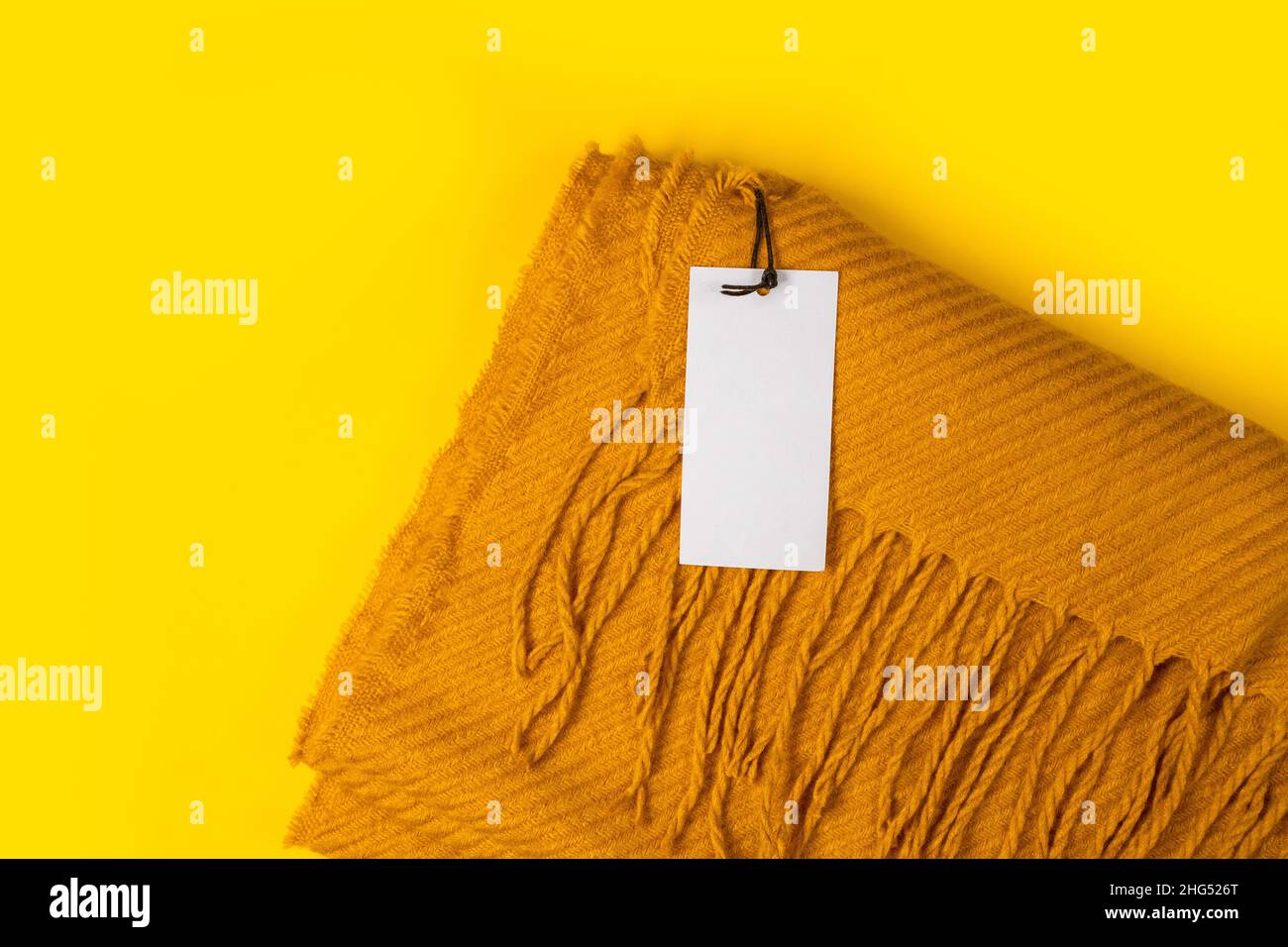 Bella sciarpa gialla calda inverno con etichetta tag mockup modello su sfondo giallo con spazio per il testo, vista dall'alto. Stagione autunnale o autunnale. Foto Stock
