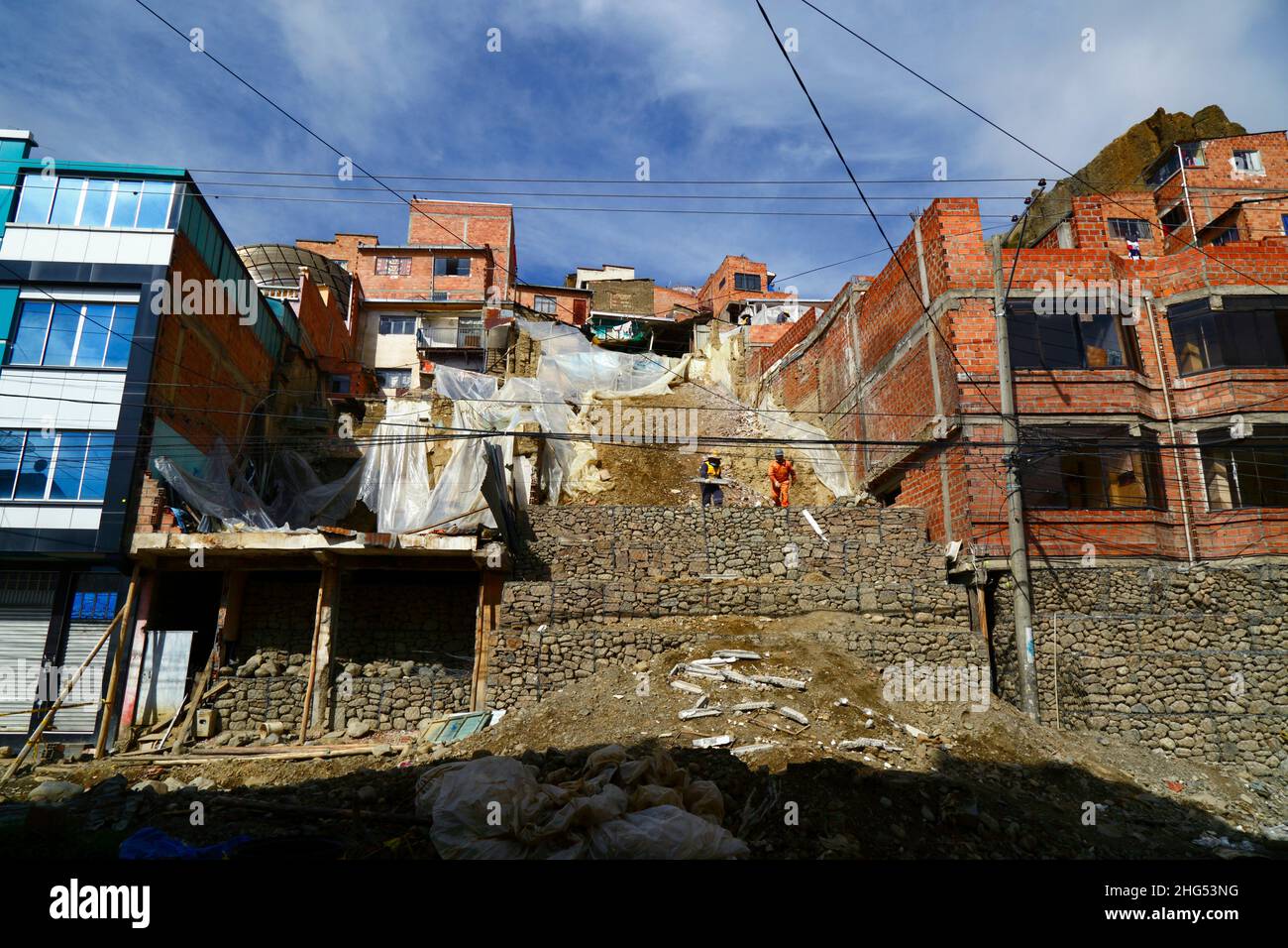 La Paz, Bolivia: Lavoratori municipali che stabilizzano una collina e case danneggiate con gabbie piene di rocce/bungalow in un sito nel distretto di Tembladerani/Cotahuma. Scavi non autorizzati e movimento terra da parte di uno dei proprietari hanno causato il crollo di parte della collina. Molti dei quartieri collinari di la Paz sono stati costruiti in aree instabili senza permessi adeguati o controlli sugli edifici. Il cedimento e l'erosione che causano frane e case crollate sono comuni, soprattutto nella stagione delle piogge. In questo incidente 2 case hanno dovuto essere demolite e altre 6 sono state gravemente colpite. Foto Stock
