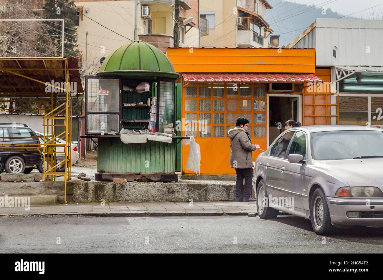 Vita quotidiana in Sud Bulgaria. Negozi vecchi e vecchi e due persone che parlano tra loro. Un'auto è parcheggiata all'esterno dei negozi. Paesi della Bulgaria meridionale Foto Stock