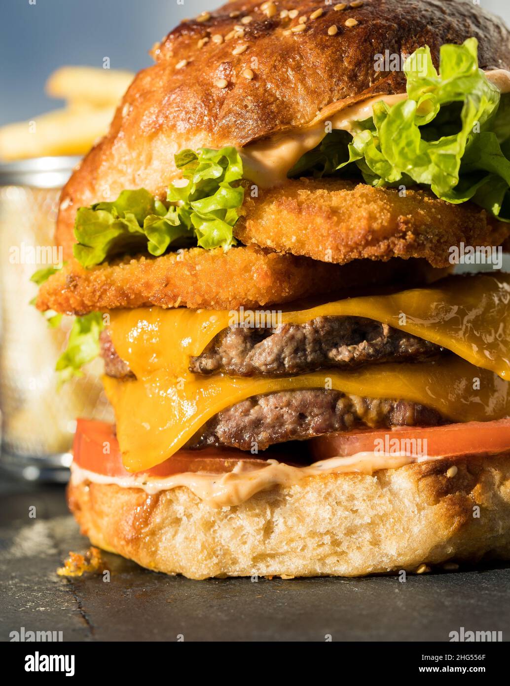 Un hamburger molto grande con due polpettine di pollo croccanti, due polpettine di carne bovina, fette di formaggio cheddar, lattuga fresca e due fette di pomodoro Foto Stock