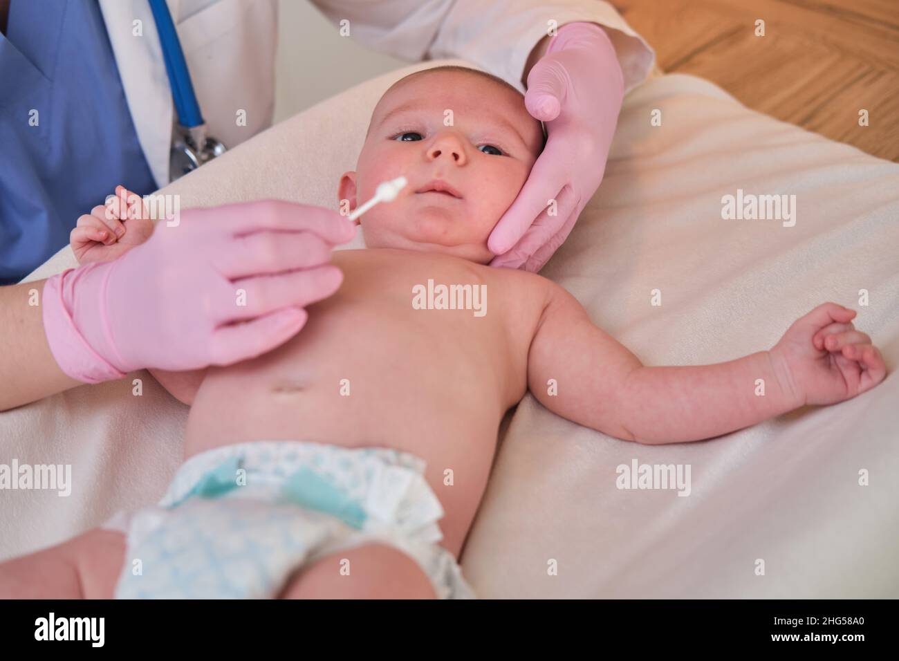 Il medico effettua l'igiene del naso e delle orecchie del neonato con un bastoncino di cotone. L'infermiera in uniforme sfrega la pelle di un bambino Foto Stock