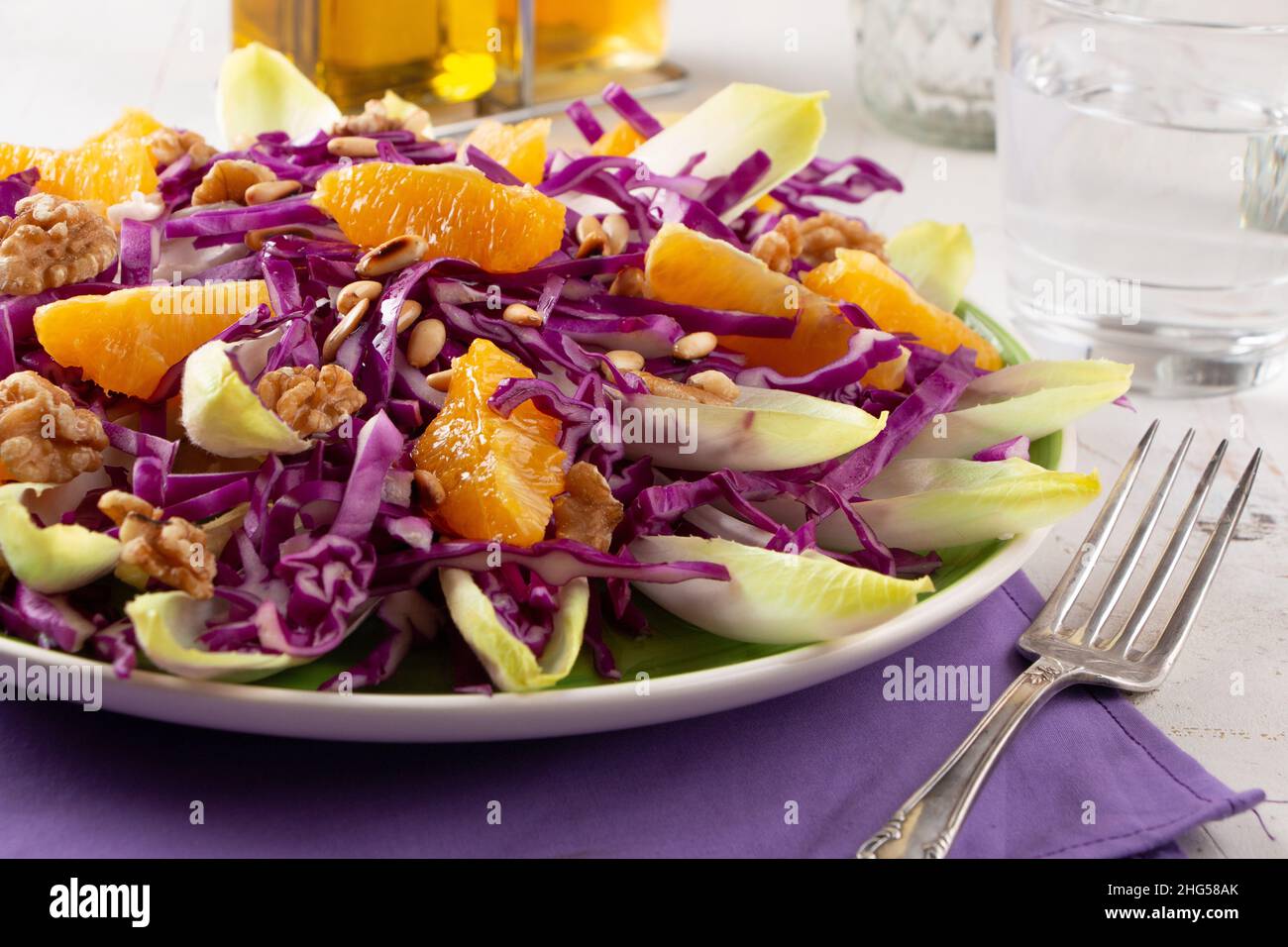 Insalata di cavolo rosso con indivia, frutta d'arancia, pinoli tostati e noci su un tovagliolo viola Foto Stock