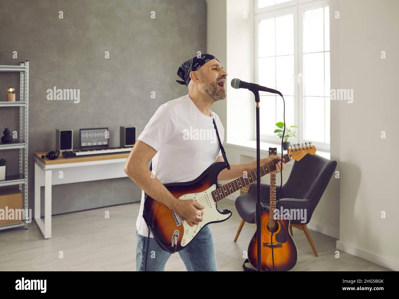 Musicista in piedi nella sala delle prove, suonando chitarra elettrica e cantando nel microfono Foto Stock