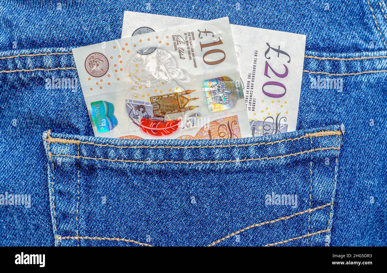 Le banconote del Regno Unito sporgono dalla tasca blu dei jeans da vicino Foto Stock