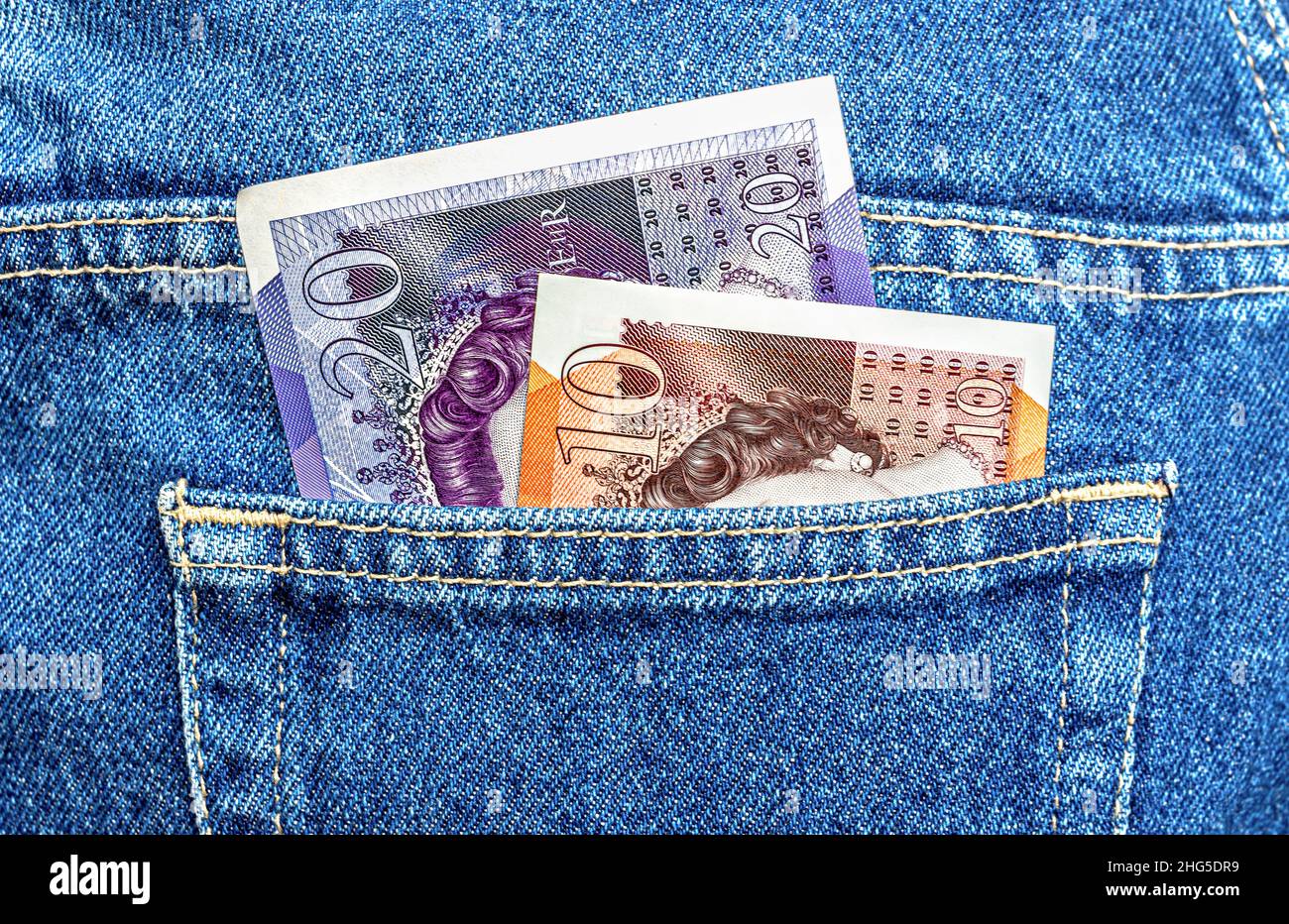 Le banconote britanniche sporgono dalla tasca blu dei jeans in primo piano Foto Stock