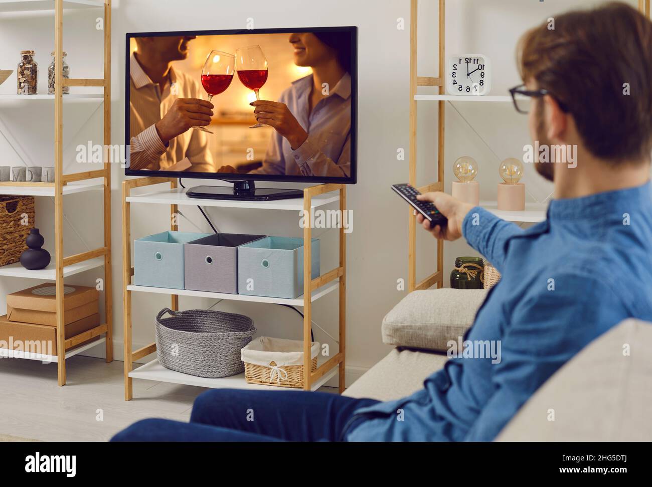 Giovane uomo seduto sul divano a casa e guardando romantica storia d'amore in televisione Foto Stock