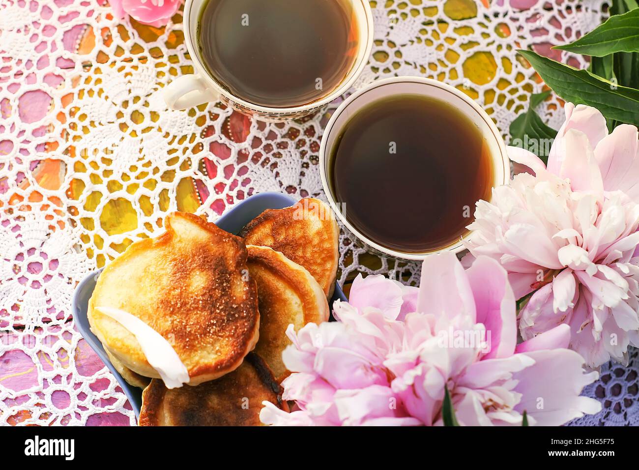 Tè in stile country nel giardino estivo nel villaggio. Due tazze di tè nero e pancake fatti a mano su tovaglie vintage crocheted e pe fiorente Foto Stock