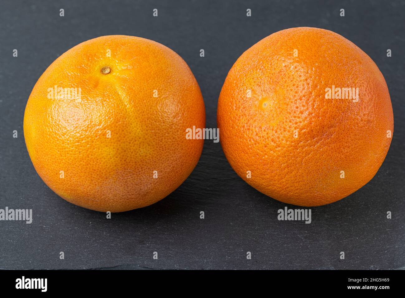 Vista ravvicinata di due pompelmi interi isolati sul tagliere nero. Foto Stock