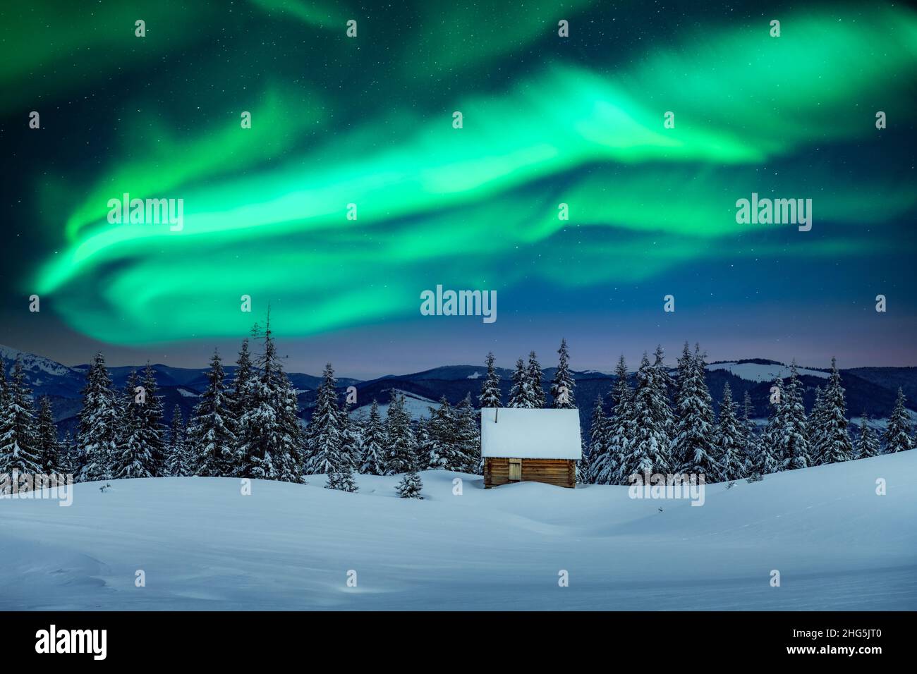 Fantastico paesaggio invernale con casa in legno in montagne innevate e luce nord nel cielo notturno. Vacanza di Natale e vacanza invernale concetto Foto Stock