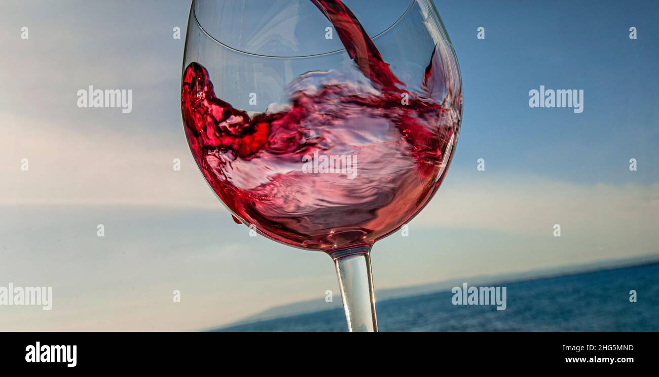 Vino rosso che si versa in vetro con ampia vacanza vista sul paesaggio marino e cielo blu vista dietro Foto Stock