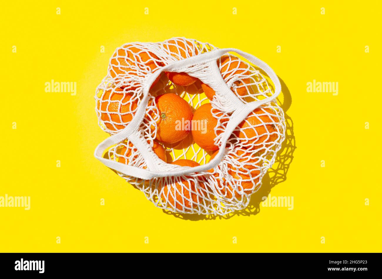 Arance in un sacchetto riutilizzabile a rete su sfondo giallo brillante. Concetto di zero rifiuti Foto Stock