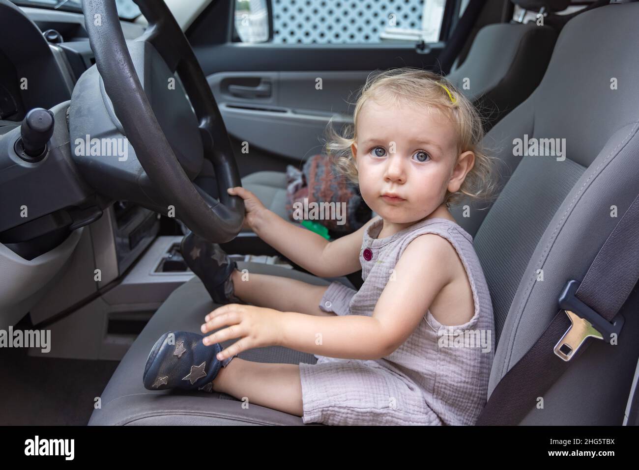 Primo piano nell'abitacolo di un veicolo a motore, mentre i giochi fantasiosi del bambino fanno credere al conducente, guardando verso la telecamera con la mano sul volante. Foto Stock