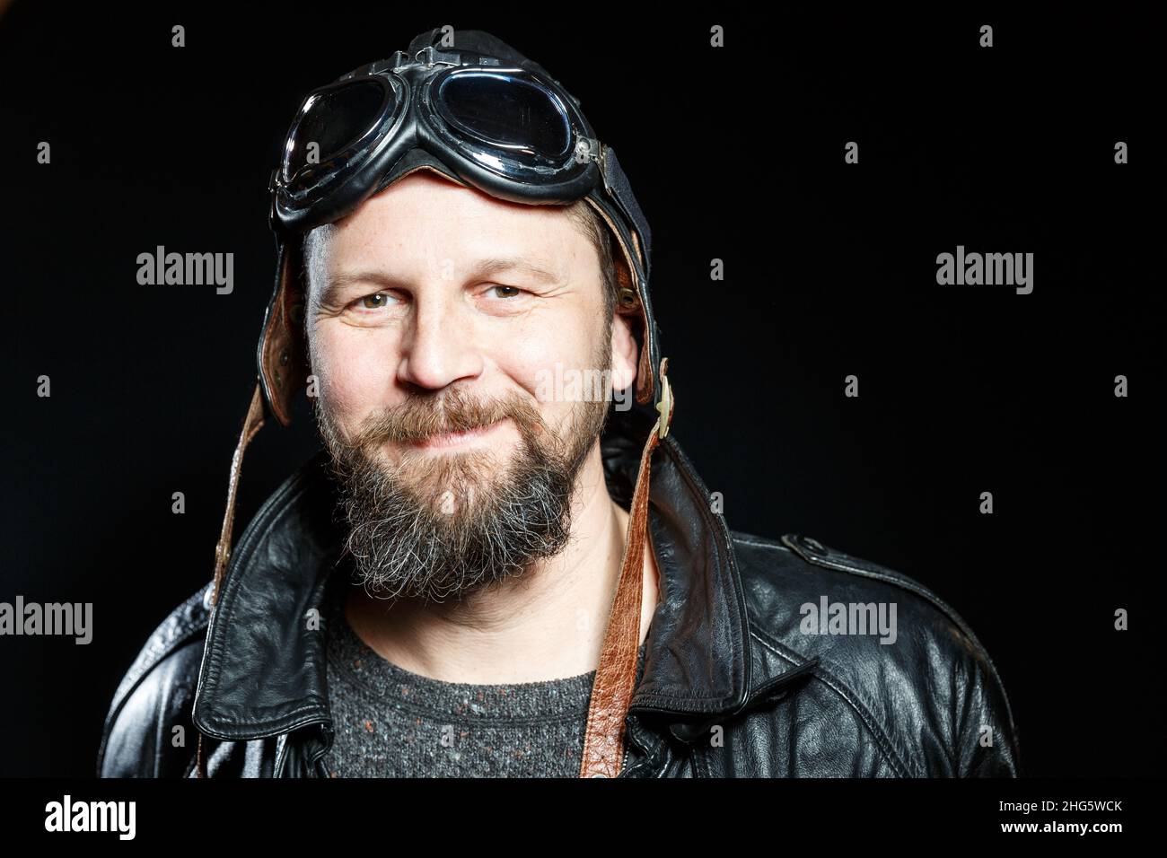 Ritratto di pilota retrò sorridente con barba che indossa occhiali vintage e casco in pelle. Concetto di nostalgia retrò automobilistica Foto Stock Ritratto di pilota retrò sorridente con barba che indossa occhiali vintage e casco in pelle. Concetto di nostalgia retrò automobilistica Foto Stock