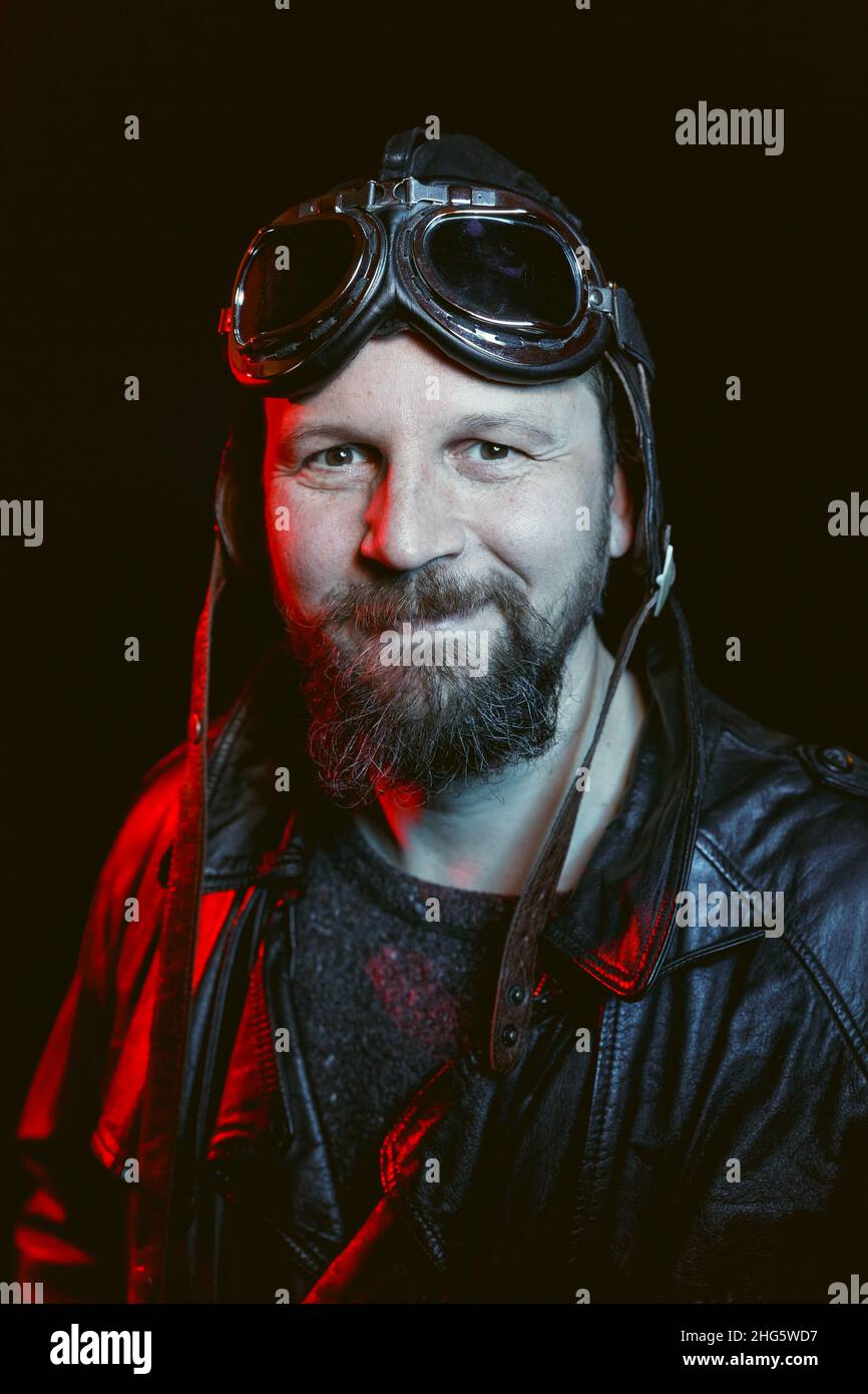 Ritratto di pilota retrò sorridente con barba che indossa occhiali vintage e casco in pelle. Concetto di nostalgia retrò automobilistica Foto Stock Ritratto di pilota retrò sorridente con barba che indossa occhiali vintage e casco in pelle. Concetto di nostalgia retrò automobilistica Foto Stock