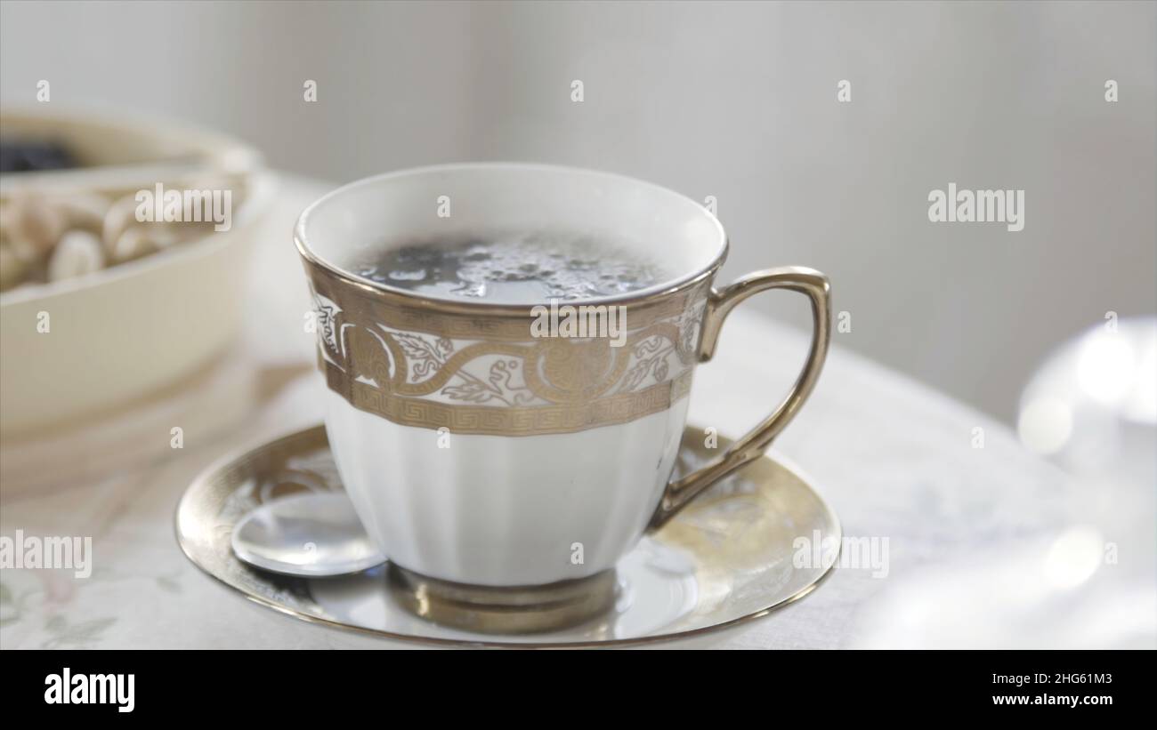 Primo piano di un'elegante tazza di tè caldo in porcellana con vapore in piedi sul tavolo in sala luminosa. Colazione mattutina aristocratica. Foto Stock