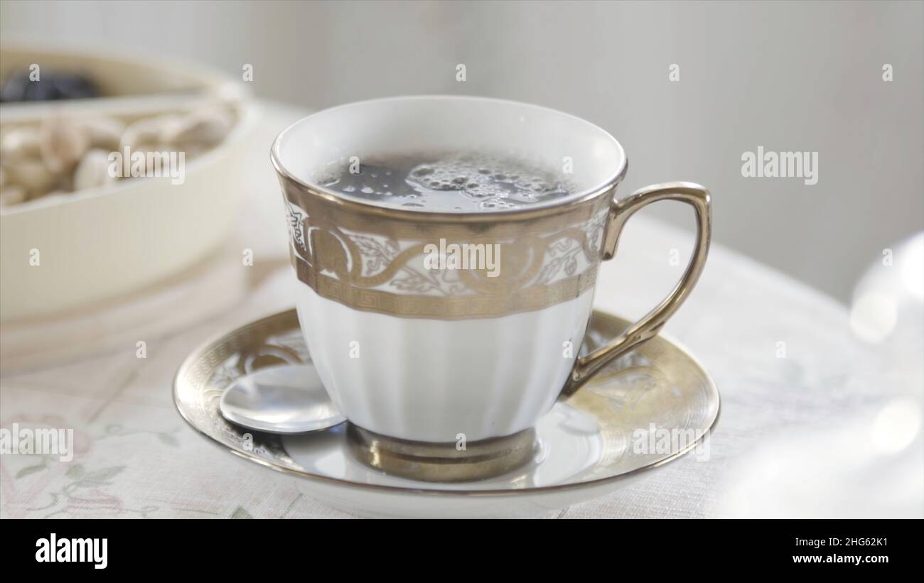 Primo piano di un'elegante tazza di tè caldo in porcellana con vapore in piedi sul tavolo in sala luminosa. Colazione mattutina aristocratica. Foto Stock
