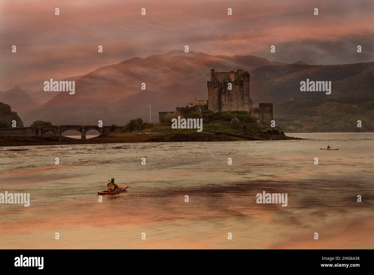 Castello di Eilean Donan al tramonto con sfumature pastello di blu e rosa che si riflettono nell'acqua con un paio di canoisti che si addossano al passato. Foto Stock