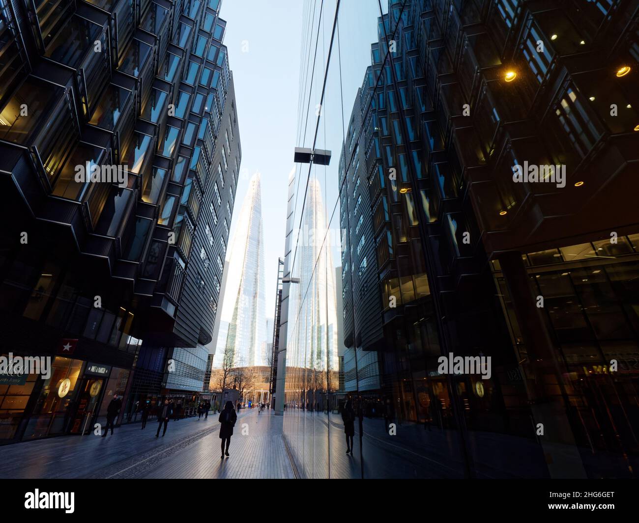 Pedoni passeggiando accanto ai negozi si riflettono nelle finestre dell'architettura moderna con il grattacielo Shard dietro, Londra. Foto Stock