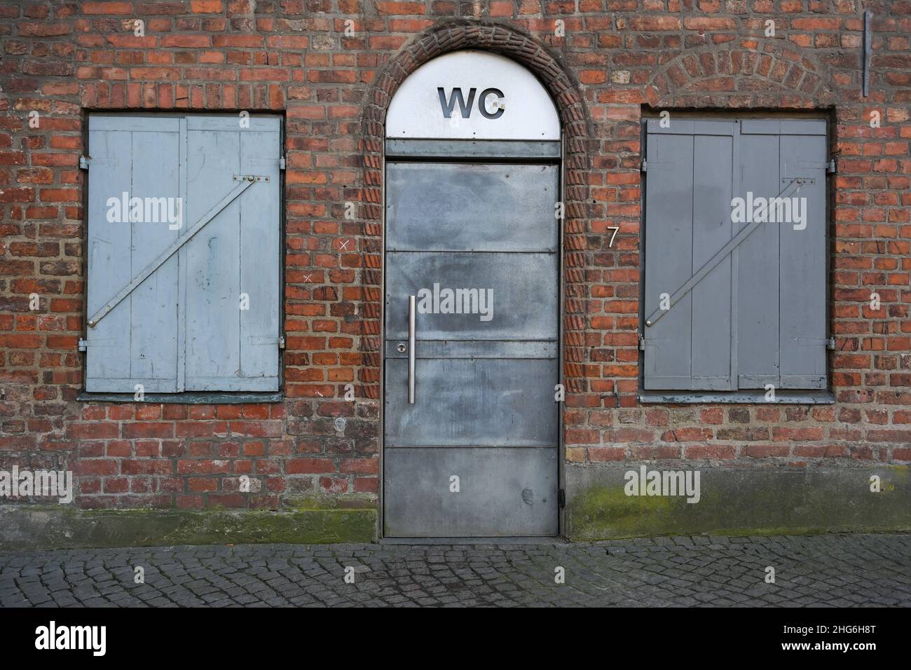 servizi igienici pubblici con una porta di metallo grigio e un cartello WC in uno storico edificio in mattoni rossi nel centro storico della città di Lubeck, Germania Foto Stock