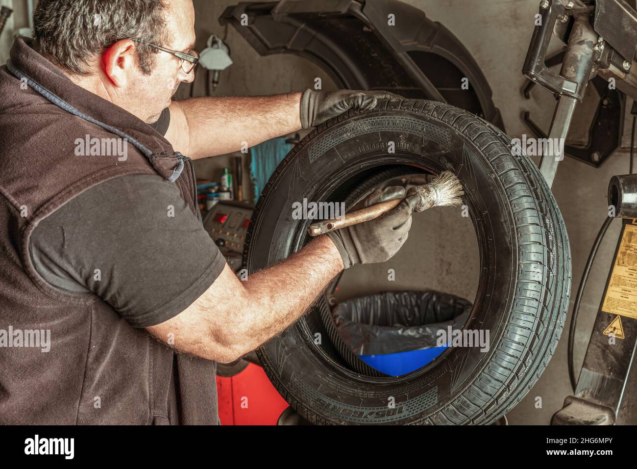 Uomo che applica lubrificante a uno pneumatico utilizzando una spazzola in un garage Foto Stock