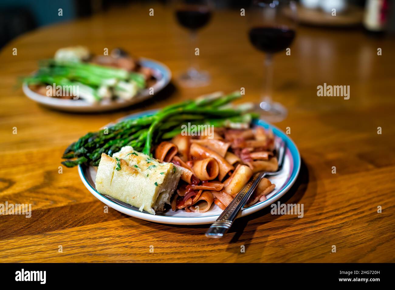 Piatto da pranzo come pasto romantico con asparagi, vino rosso salsa di pomodoro rigatoni pasta su tavola di legno con pane all'aglio, forchetta e nessuno bokeh sfondo Foto Stock