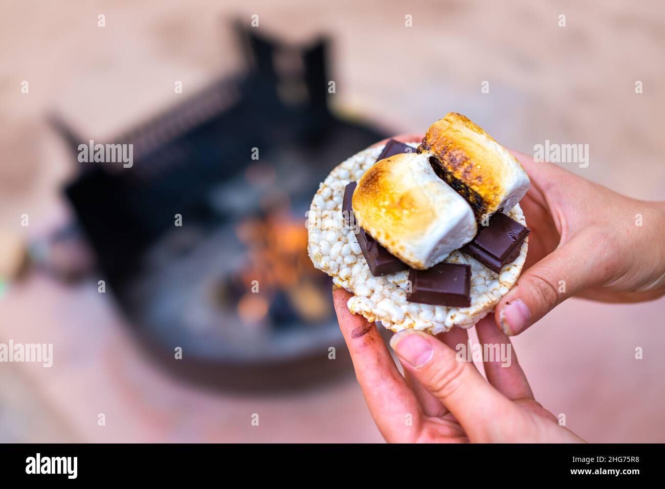 Giovane donna campeggio closeup mano che tiene marshmallows arrostiti smores con tavolette di cioccolato e cracker torta di riso da fuoco buca in campeggio campfi Foto Stock