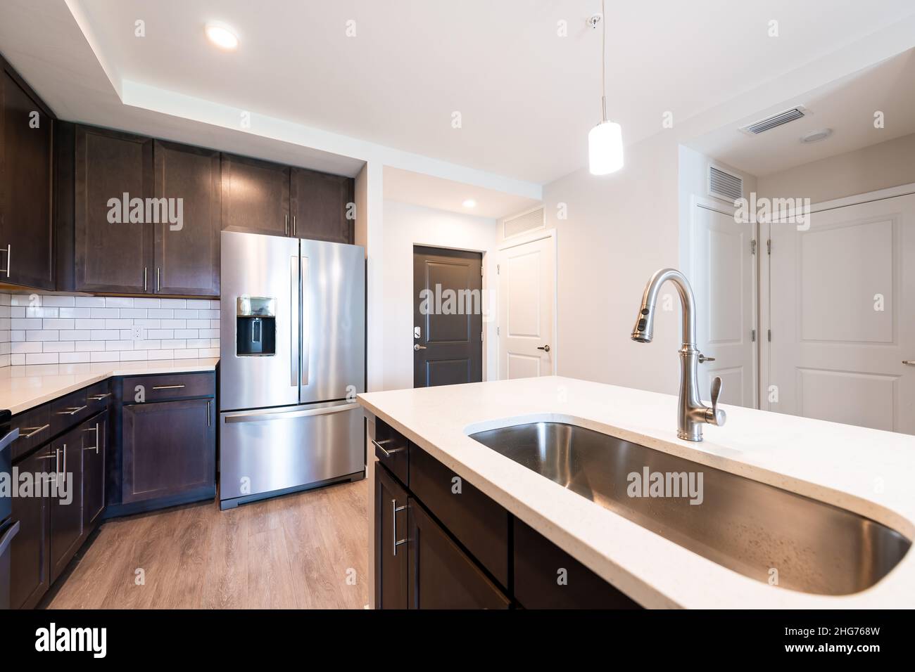 Cucina vuota moderna casa appartamento con lavello rubinetto quarzo countertop isola da nuovo frigorifero frigorifero mobili in legno e lampada a soffitto incassata Foto Stock