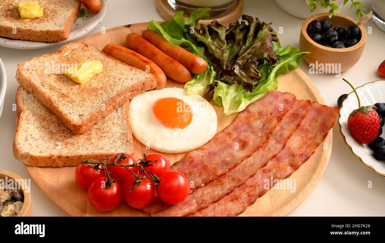 Primo piano, un piatto di una sana colazione con uova soleggiate, bacini alla griglia e salsicce, toast e verdure fresche. Foto Stock