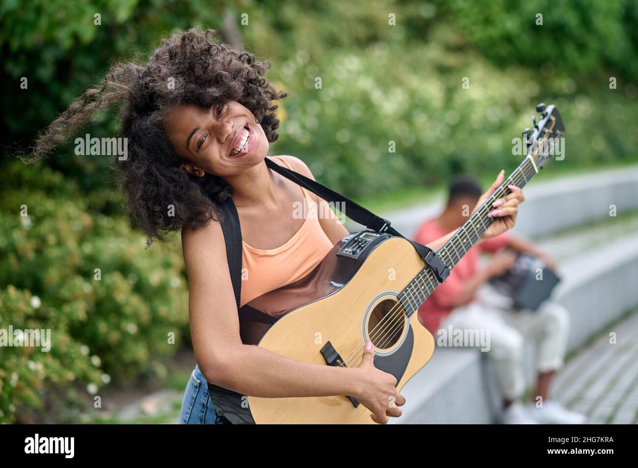 Donna felice con la chitarra e l'uomo dietro nel parco Foto Stock