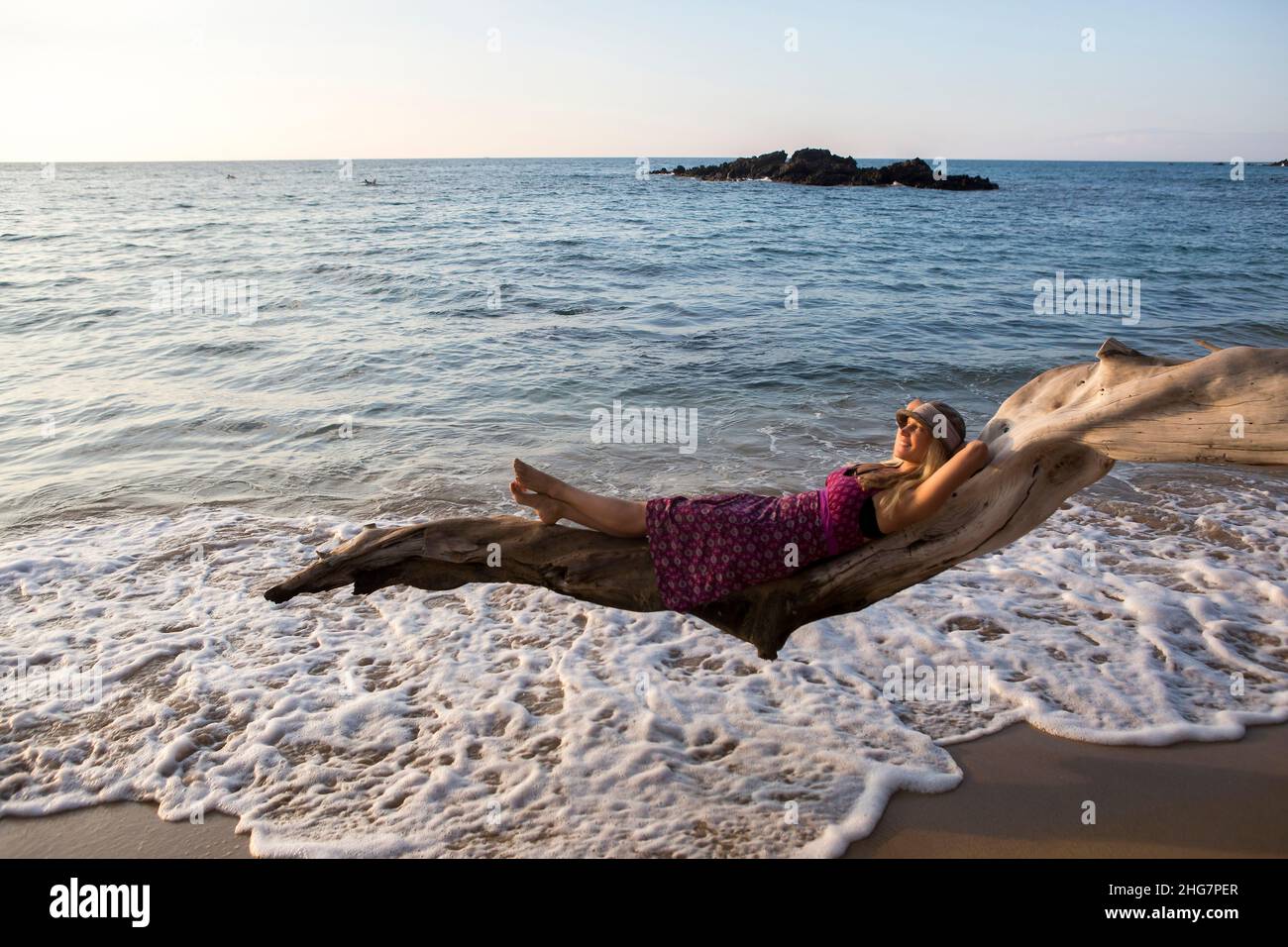 Donna sdraiata su ramo di albero sulla spiaggia tropicale Hawaiiana Foto Stock