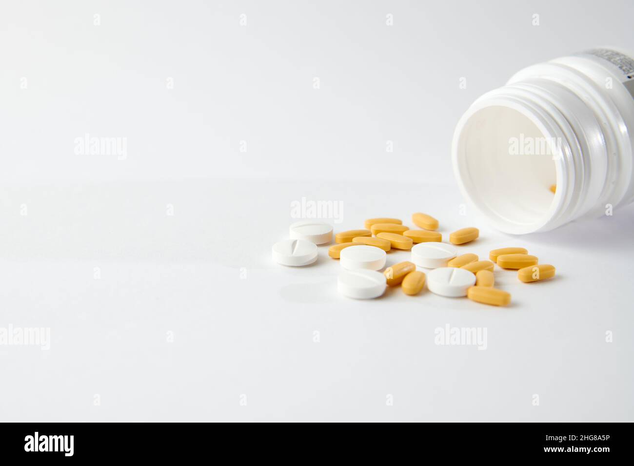 Un closeup di pillole bianche e gialle goccia fuori il flacone della pillola sulla superficie bianca Foto Stock