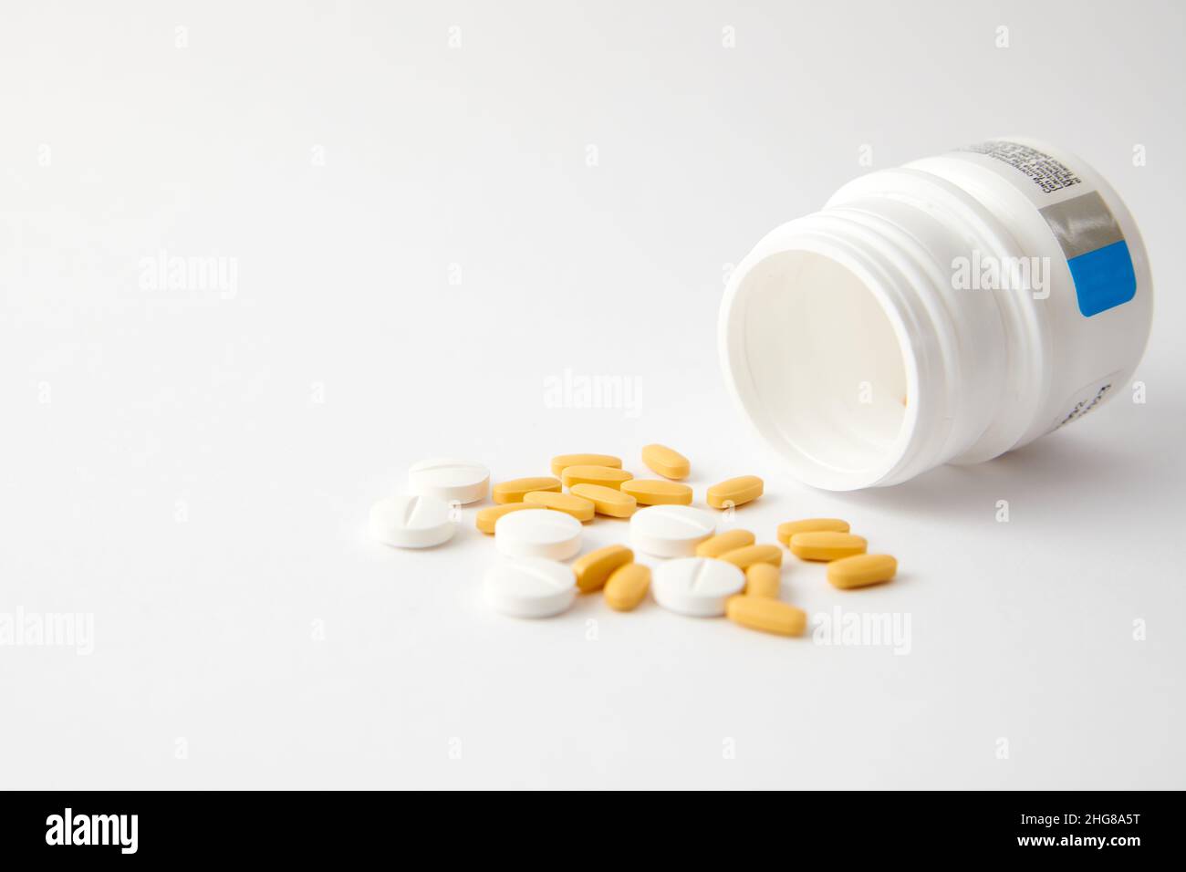 Un closeup di pillole bianche e gialle goccia fuori il flacone della pillola sulla superficie bianca Foto Stock