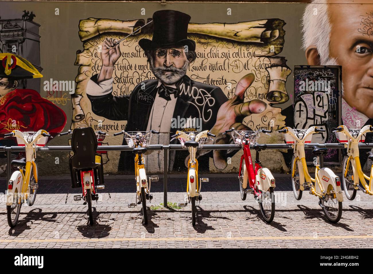 Noleggio biciclette allineate di fronte a una parete di colorati graffiti fantasiosi con temi storici. Foto Stock Noleggio biciclette allineate di fronte a una parete di colorati graffiti fantasiosi con temi storici. Foto Stock