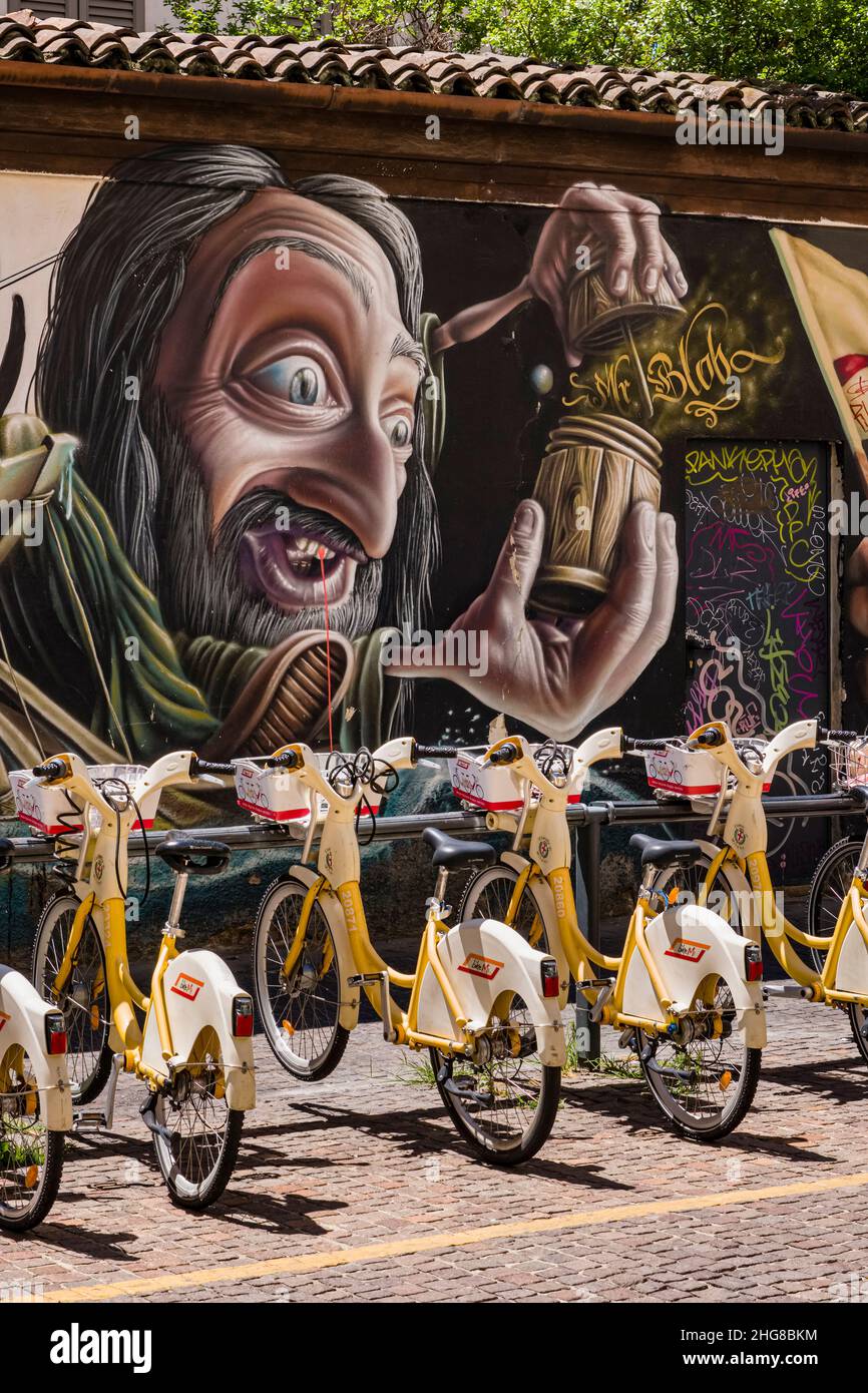 Noleggio biciclette allineate di fronte a una parete di colorati graffiti fantasiosi con temi storici. Foto Stock Noleggio biciclette allineate di fronte a una parete di colorati graffiti fantasiosi con temi storici. Foto Stock